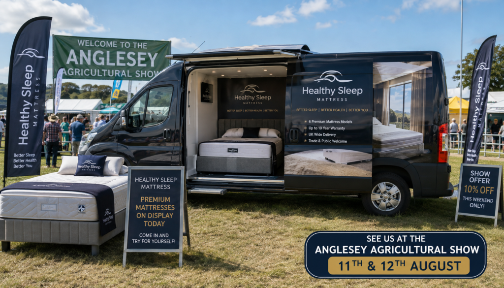 Black van converted into a bedroom showroom at an outdoor fair, with a bed on display and large Healthy Sleep banners nearby.